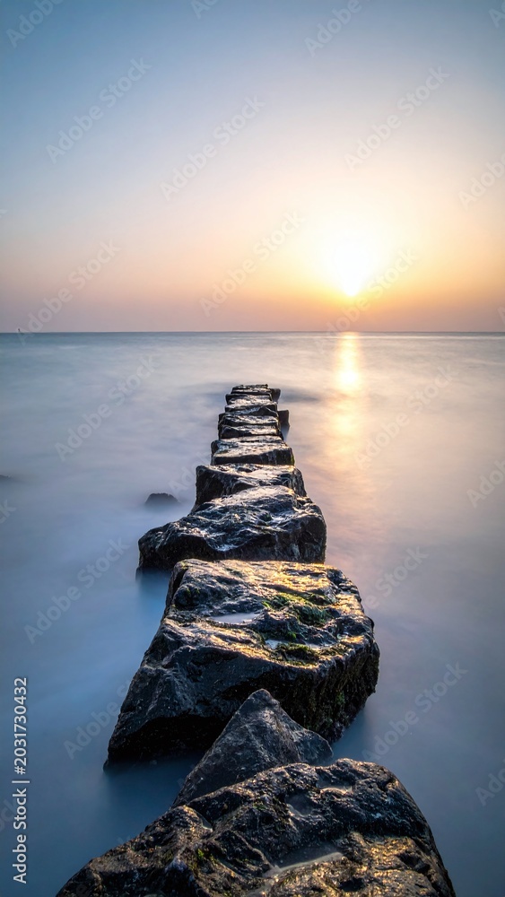 Obraz premium Experience tranquility with this long exposure coastal landscape. Stone rocks lead into a misty sea under a golden sunrise, symbolizing focus, paths, and inner peace in wild nature.