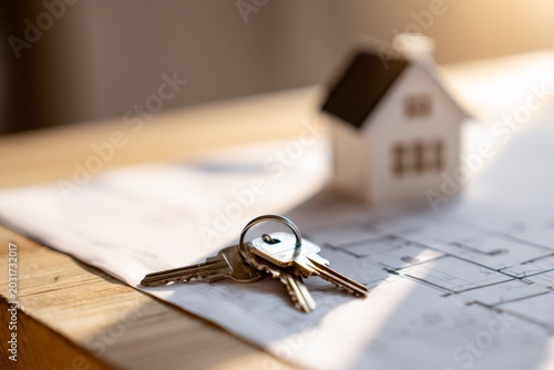 House keys on an architectural blueprint with a model home in the background. Real estate  property purchase  and mortgage concept for a new home
