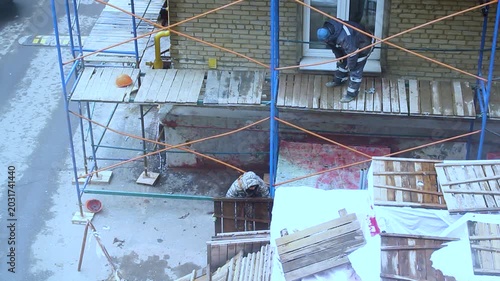 Construction workers moving wooden planks on scaffolding near brick building