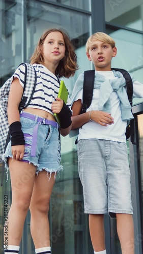 School students, teenage boy and girl standing near a building of school on the stairs talking during break time at bright summer day, outdoors. Slow motion