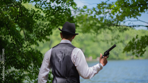 фотографія Retro gangster with revolver near lake in suspense concept with copy space