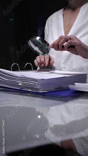 Businesswoman conducting detailed audit checking financial spreadsheets using magnifying glass with laptop and documents on desk. Audit and taxes concept