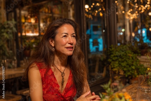 beautiful woman is sitting at table in restaurant. She's talking or giving interview. She's well dressed. pleasant lively atmosphere around. photo conveys business conversation or meeting of friends
