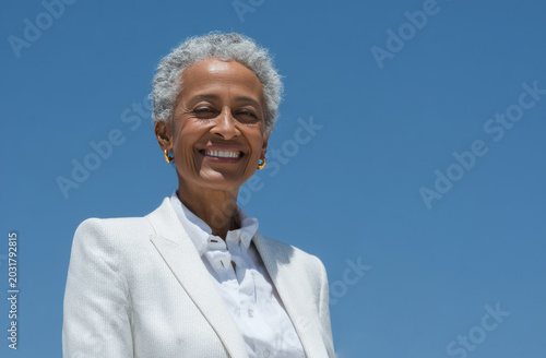 60 yo  female financial executive of a silicon valley startup wearing white blazer and white shirt taking a black credit card out of his front pocket while smiles confidently to the camera. 