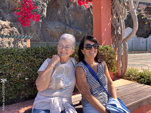 Photos Two Senior Women Friends Smiling on Bench in Sunny Garden With Bougainvillea Flo