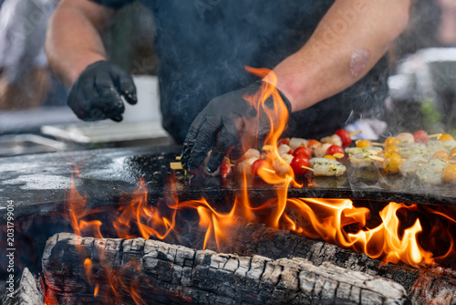 Préparation de brochettes de fruits de mer sur brasero avec cuisson au feu de bois et fumée en extérieur.