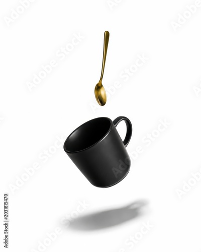 Matte black espresso cup and a small gold spoon falling down in a balanced vertical composition dramatic suspended motion clean shadow stretching beneath the objects isolated