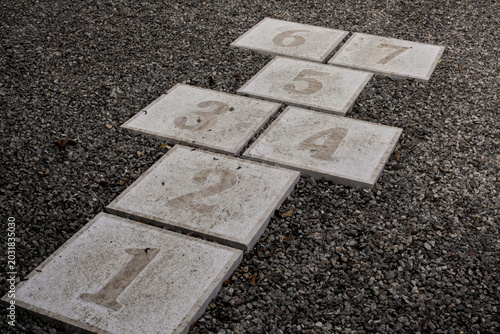 Foto Permanent outdoor hopscotch court with numbered concrete pavers (1-7) embedded in a gravel surface
