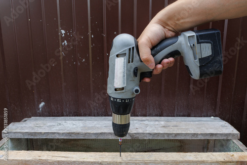 Tableau sur toile Side view of a hand holding a grey cordless drill vertically above a wooden box