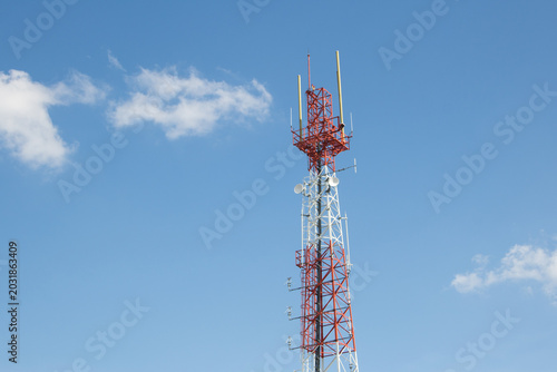 A Tall Red and White Telecommunication Tower Equipped with Sector Antennas and Satellite Dishes Standing Tall Against a Bright Blue Sky with Soft Clouds