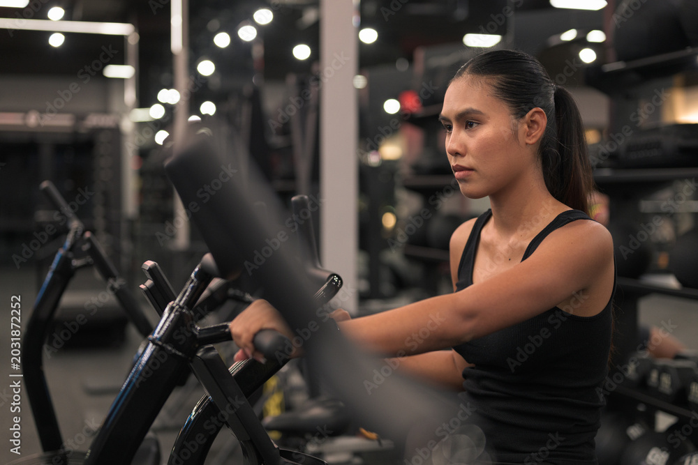 Fototapeta premium Determined Asian Woman Working Out on Air Bike at Gym at Night