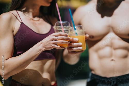 Tableau sur toile Fit young couple in athletic wear hold plastic cups of orange juice