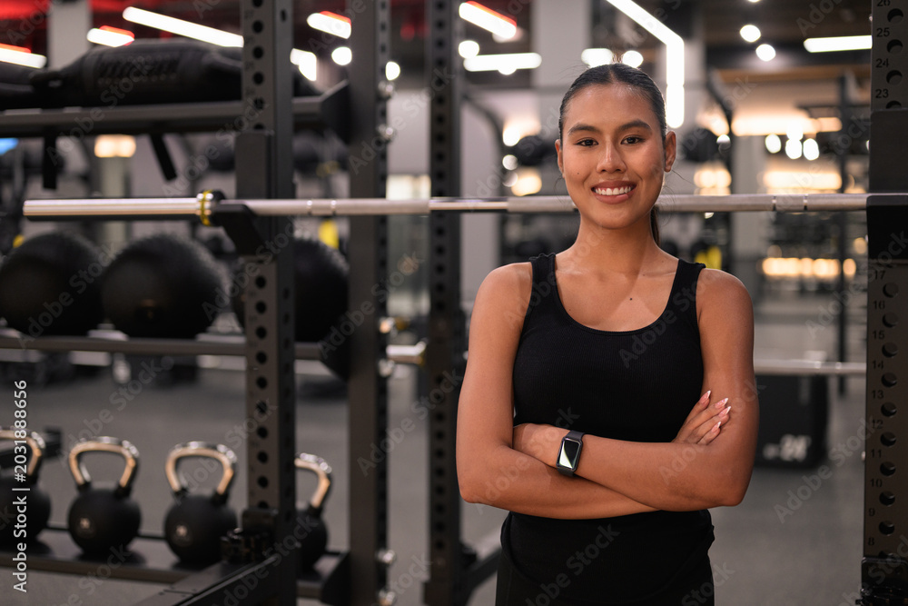Fototapeta premium Asian Thai Isan Woman Smiling with Crossed Arms at Gym at Night