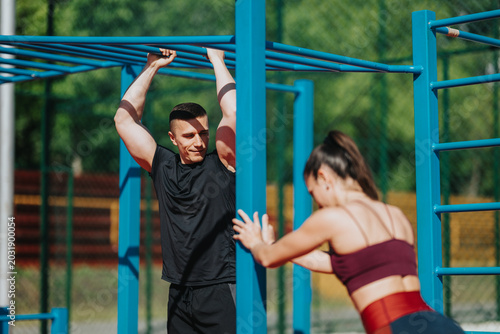 Canvas Print A young man and woman train on blue outdoor monkey bars performing strength exercises