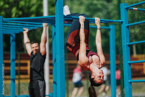 Photography A fit woman hangs upside down from blue monkey bars while exercising outdoors