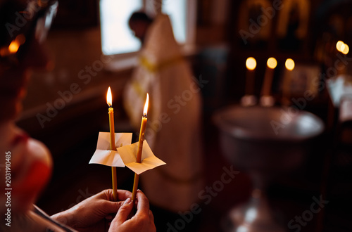 Bild auf Leinwand Close up of hands holding lit candles during an Orthodox baptism ceremony, with soft focus church interior and warm candlelight