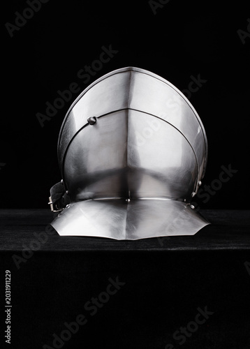 Cuadro en lienzo Front view of polished medieval steel helmet with pointed visor and neck guard on black backdrop