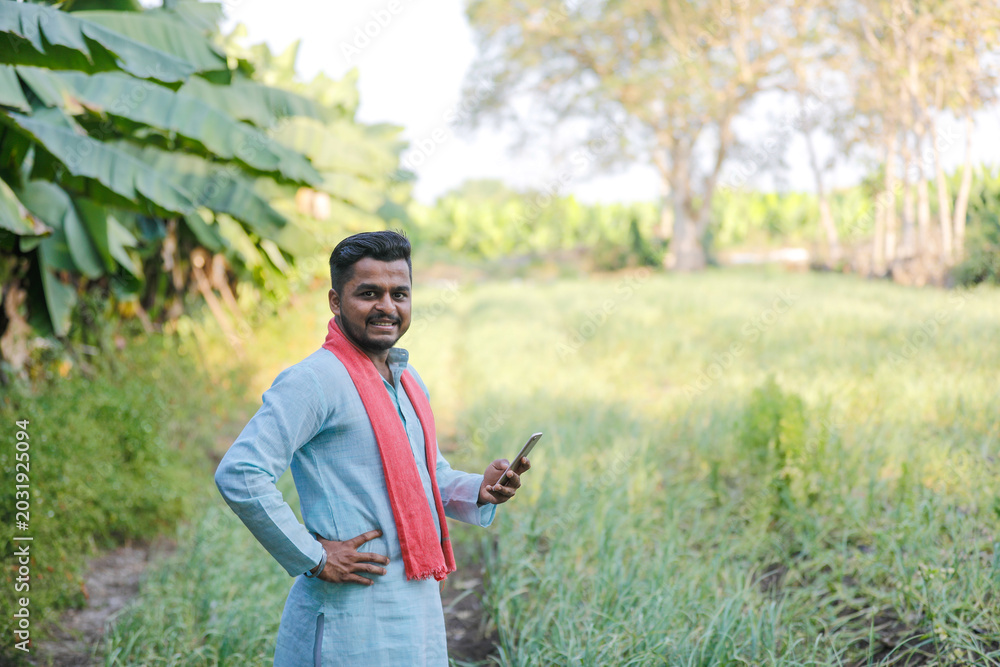 Fototapeta premium young indian farmer using smartphone standing at agricultural field