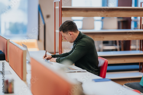 Photos A businessman sits at a desk working on documents with a laptop in a modern office