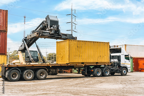 Reach stacker loading yellow shipping container onto truck at industrial terminal port