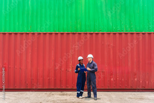 Diverse male and female logistics engineers consulting and inspecting shipping container and coordinating delivery schedules at industrial port terminal