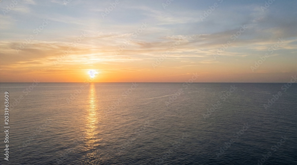 Obraz premium Serene ocean sunset with golden sun and calm water.