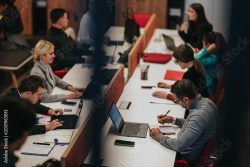 Fotografie Business professionals collaborate at a long shared desk, using laptops and taking notes