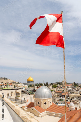 Waving Austrian flag in front of Jerusalem Old City as seen from Austrian Hospice. View at Church of Our Lady of Sorrows, Dome of the Rock on the Temple Mount and Al-Aqsa Mosque