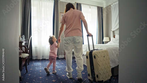 Fotografie Mother and young daughter arrive at an elegant hotel suite, pulling a suitcase a