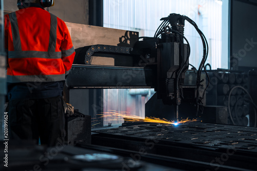 Valokuva Professional operator worker monitoring automated cnc plasma machine cutting heavy steel metal plate with bright sparks