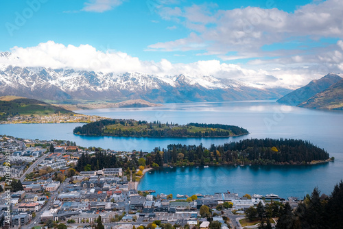 Queenstown, New Zealand: High angle panoramic overview of the lakefront town and green peninsula at Lake Wakatipu, a travel vista under cloudy skies.