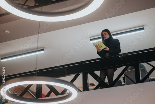 Canvastavla A businesswoman reads a notebook while standing on a mezzanine balcony in a modern office