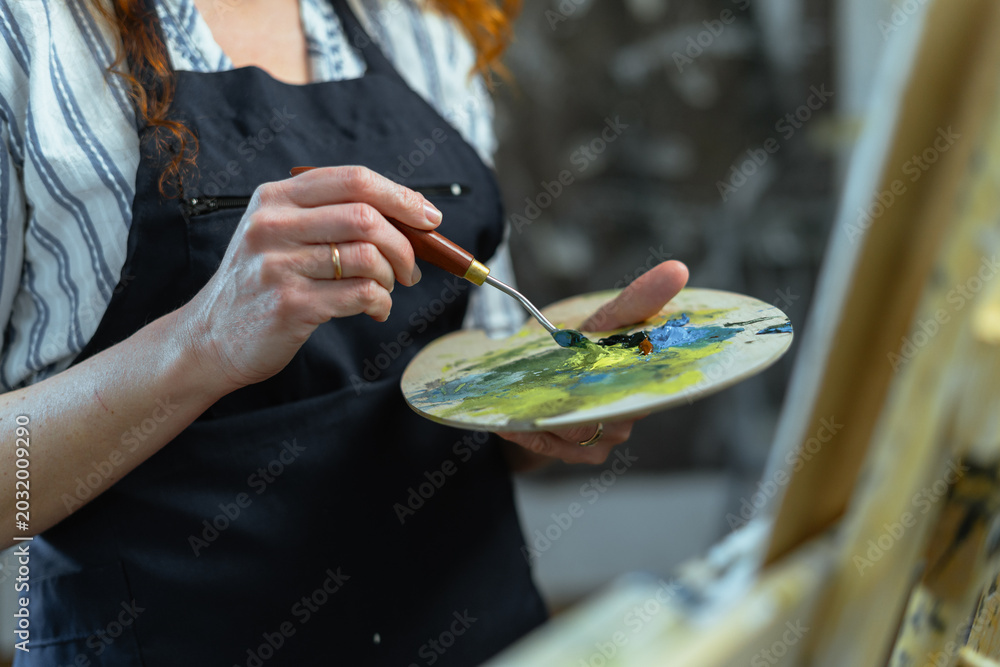 Obraz premium Female artist holding paintbrush and palette indoors