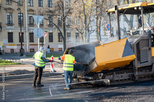 Foto Road workers in vests using shovels tools to scoop fresh hot asphalt from paver machine onto road surface to evenly distribute material over ground surface, roadwork and street repair working process