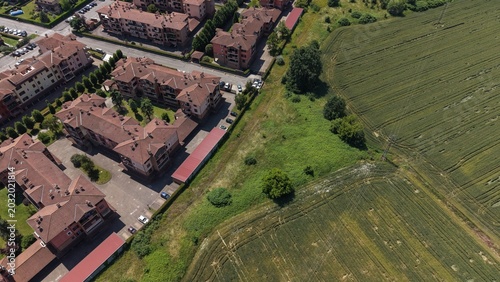 Quadro su tela Aerial View of Urban Expansion: A modern residential area with terracotta-roofed buildings stands adjacent to a vibrant green agricultural field