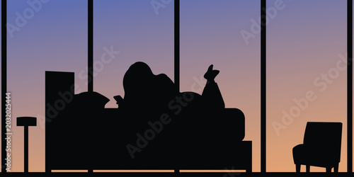 Silhouette of a person relaxing on a couch in front of a large window at sunset