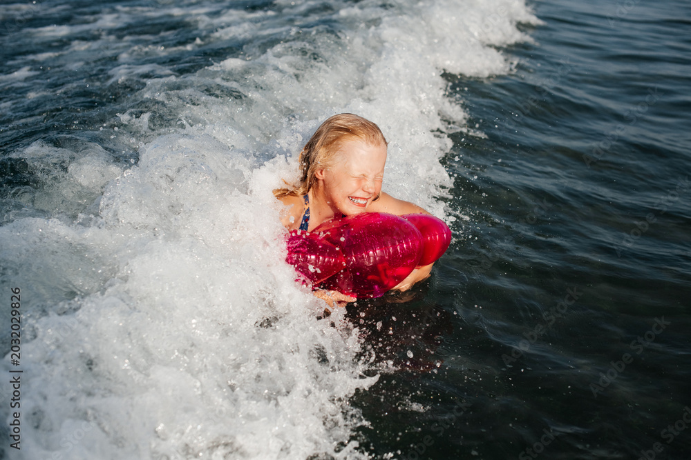 Fototapeta premium Laughing teenage girl riding breaking wave on pink inflatable ring