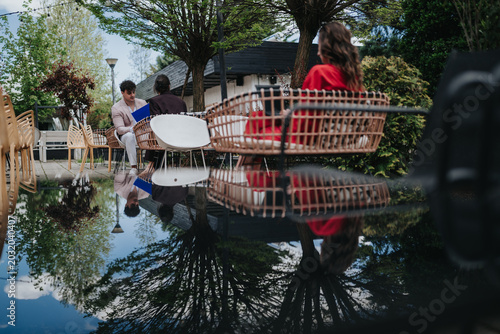 Bild auf Leinwand Two colleagues discuss documents while seated at an outdoor cafe beside a reflective water surface
