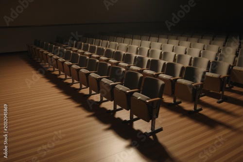 Rows of empty theater seats in a dimly lit auditorium feature wooden armrests and metal bases under warm lighting.