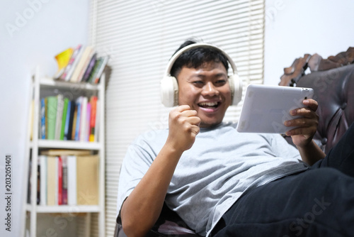 Φωτογραφία A cheerful Asian man is having fun playing video games on his smartphone while comfortably lying on a sofa