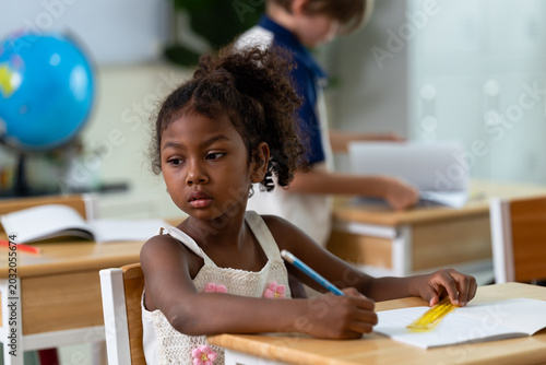 Εκτύπωση καμβά Elementary girl studies notebook with pencil and ruler at desk while classmate works behind, back to school classroom routine supports writing practice, attention, confidence, study discipline