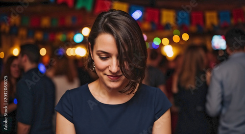 Shy woman at party in dim room with colorful string lights illuminating blurred crowd. Young shy woman at party stands quietly, appearing thoughtful amidst vibrant social gathering.