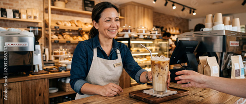 Friendly barista serving iced coffee drink at cafe counter.