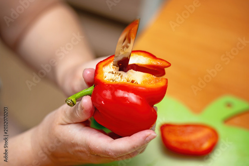 Female hands slicing red bell pepper with a vintage metal knife. Home cooking and vegetable preparation