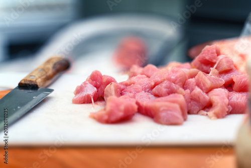 Red meat cut into cubes on a white plastic cutting board next to a chef's knife. Raw ingredient for cooking