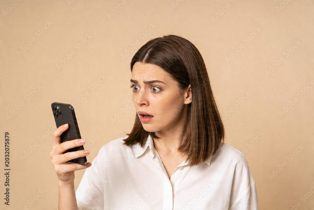 Naklejka premium Young woman reacts with shock and disbelief to something on her smartphone screen