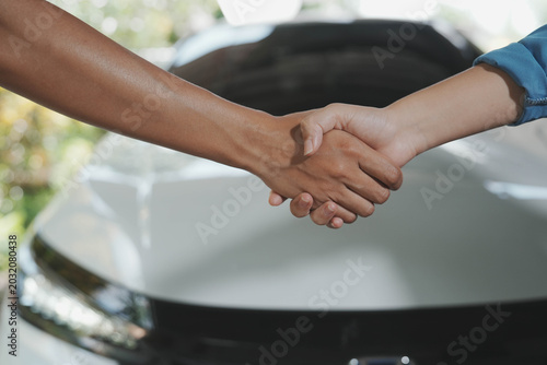 Canvas Print Two people shaking hands in front of a car, suggesting a successful vehicle purchase or service agreement at a dealership or garage