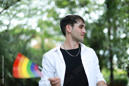 Caucasian strikingly healthy man with short hair handsome and somewhat effeminate is waving pride flag representing his sexual diversity and LGBTQ identity man who is attracted to other men.