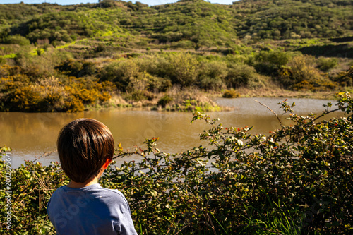Billede på lærred Child stands quietly near bushy riverbank