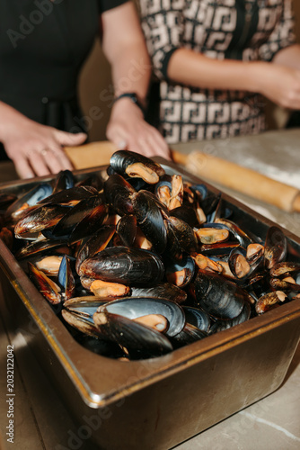 Large tray of fresh cooked mussels in shells on a kitchen counter.